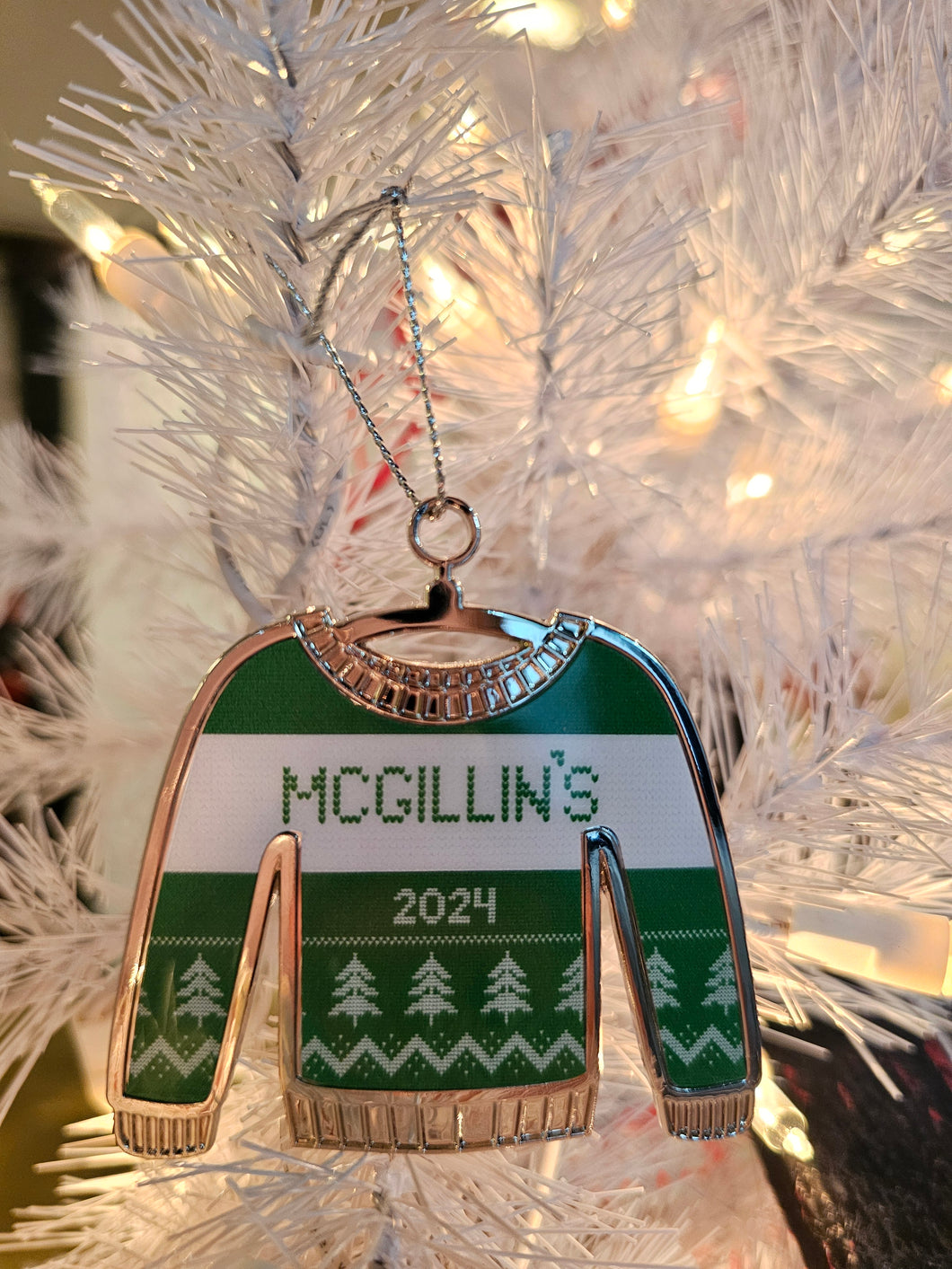 A festive green and white striped sweater ornament with 'McGillin's 2024' printed on it, hanging on a Christmas tree.