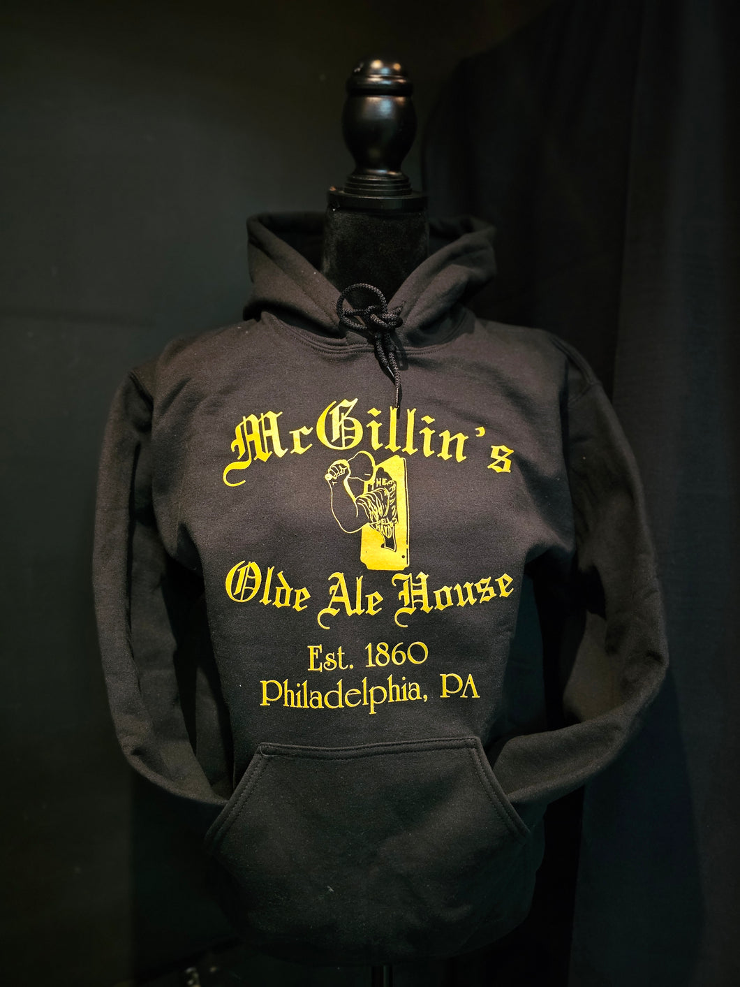 A black hoodie with 'McGillin's Olde Ale House' text and the bell in hand logo in yellow on the front.