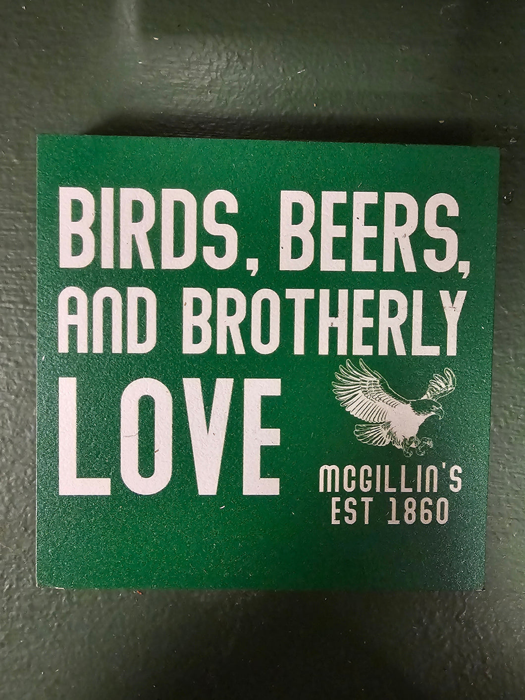 Green coaster with white text and logo on a dark surface