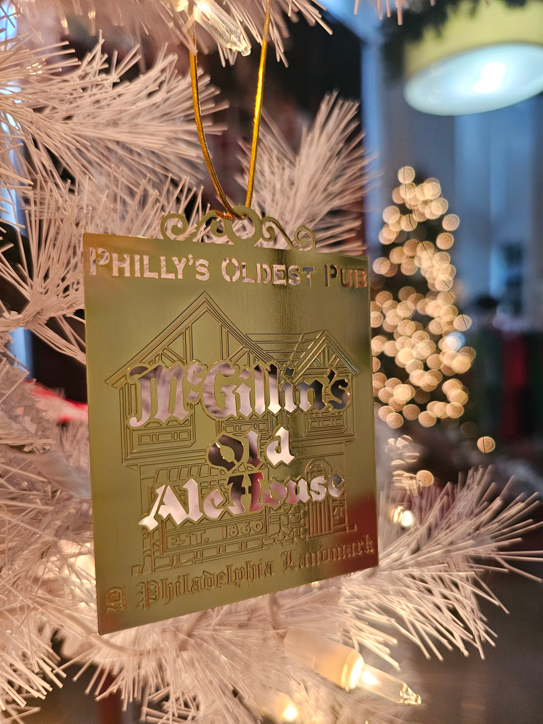 A gold etched ornament hanging on a white Christmas tree with the text 'McGillin's Olde Ale House' displayed.