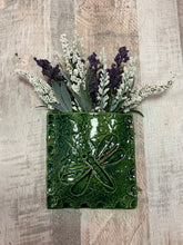 Green ceramic wall pocket with dragonfly design holding flowers hangs on wall