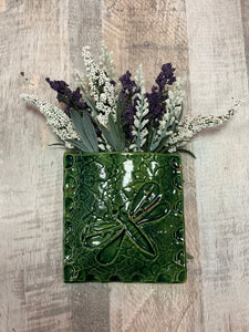 Green ceramic wall pocket with dragonfly design holding flowers hangs on wall