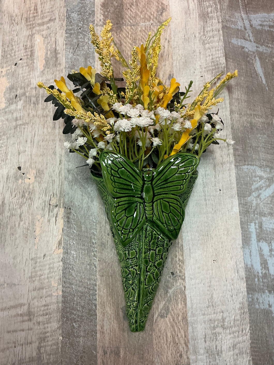 Green butterfly-shaped wall vase with flowers on a wooden background