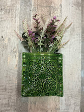 Green textured wallpocket with artificial plants hangs on wall