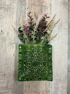 Green textured wallpocket with artificial plants hangs on wall