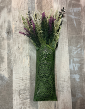 Decorative green vase with floral arrangement on a wooden background hangs on wall

