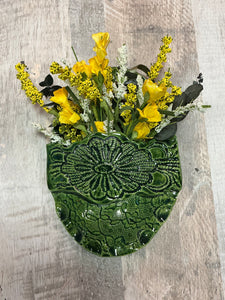 Decorative green ceramic wallpocket  vase with yellow flowers hangs on wall